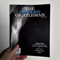 Book titled 'The Modern Gentleman' held by a hand against a light gray background