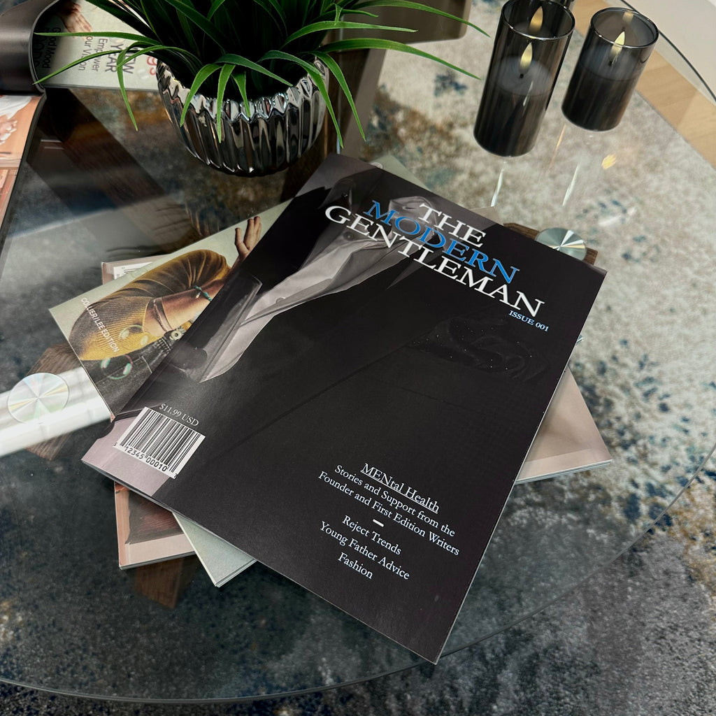 Magazine titled 'The Modern Gentleman' on a glass table with candles and a plant in the background.