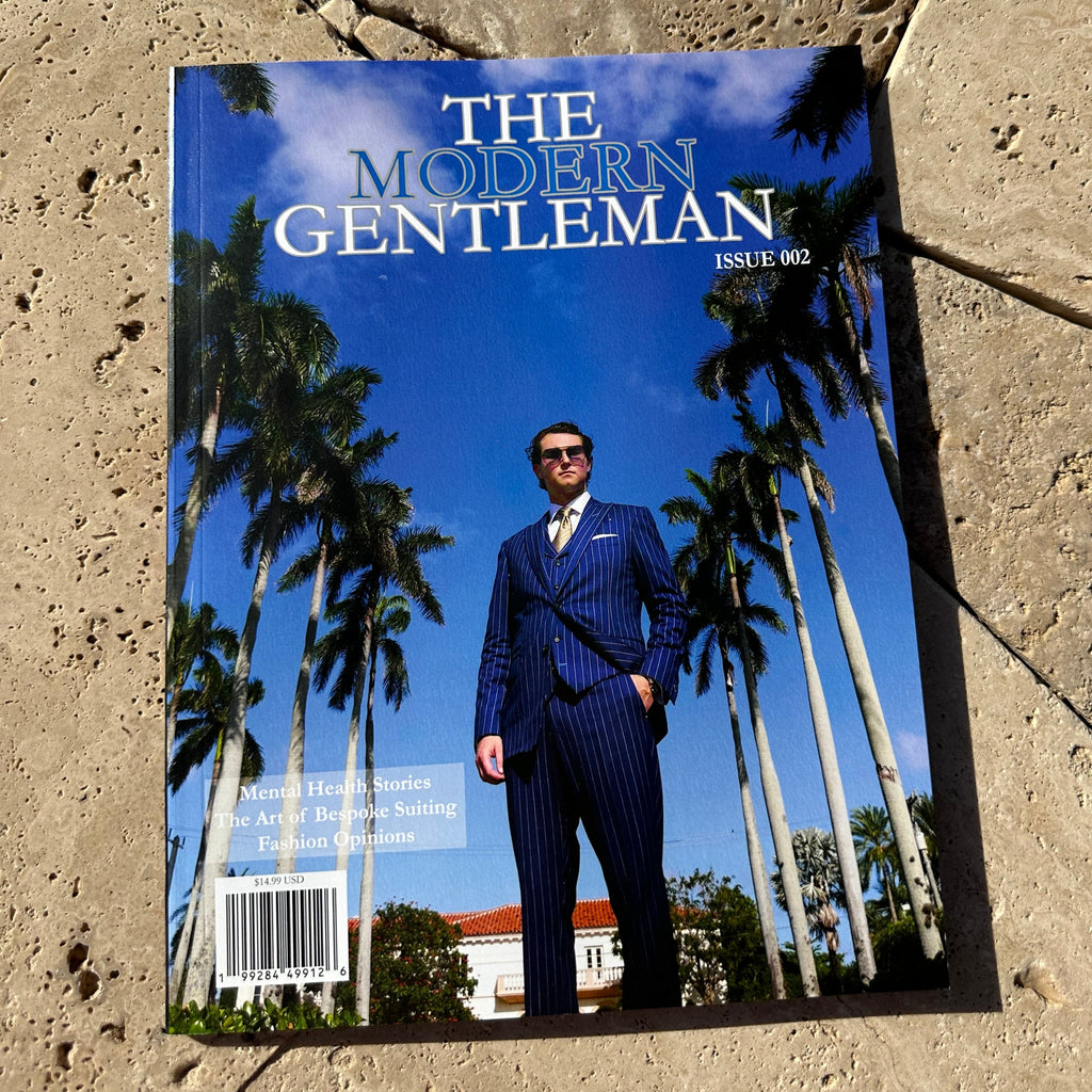 Magazine titled 'The Modern Gentleman' on a stone surface with palm trees in the background.