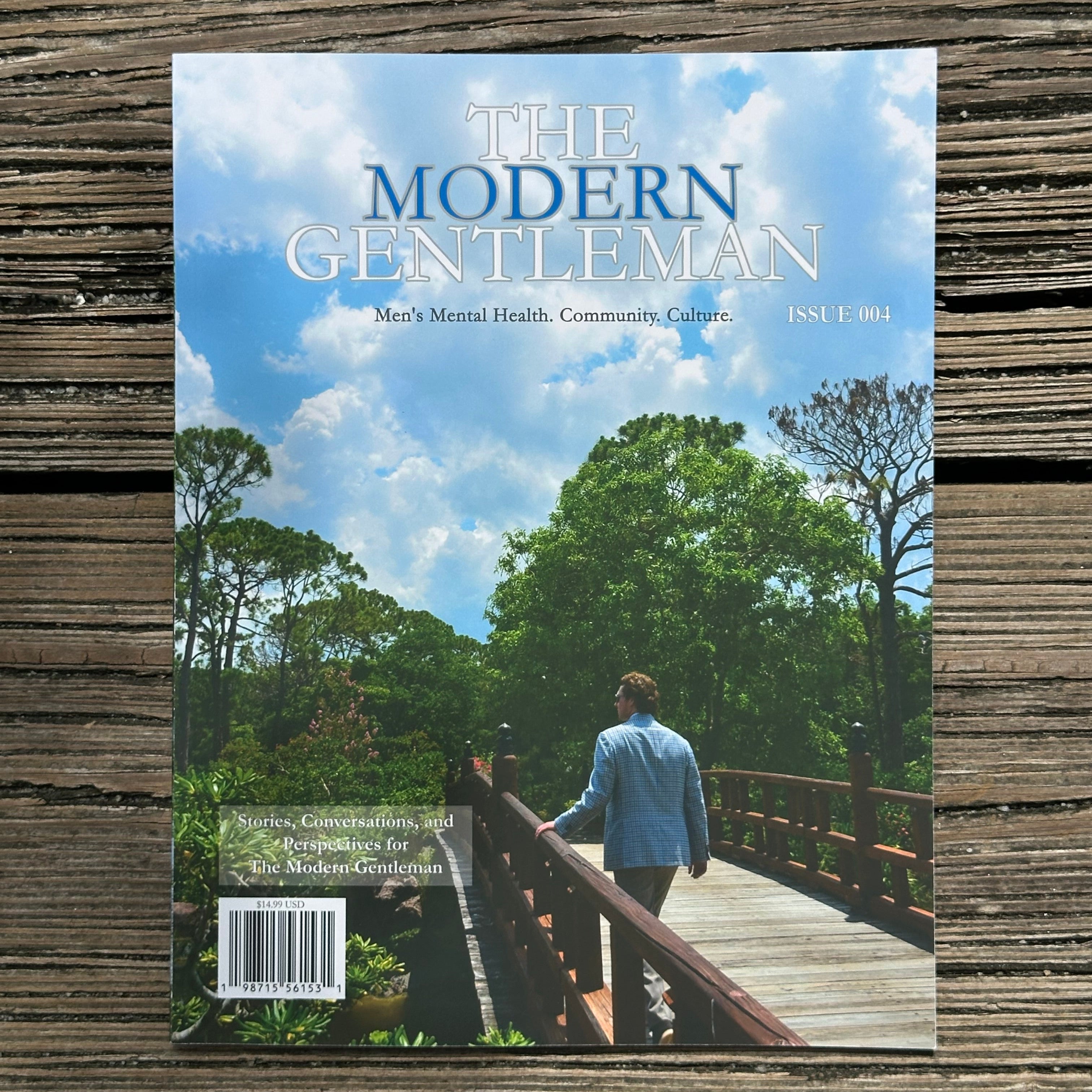 The Modern Gentleman magazine, Issue 004, featuring a cover photo of a man walking on a wooden bridge under a blue sky, displayed flat on a rustic weathered wood background.
